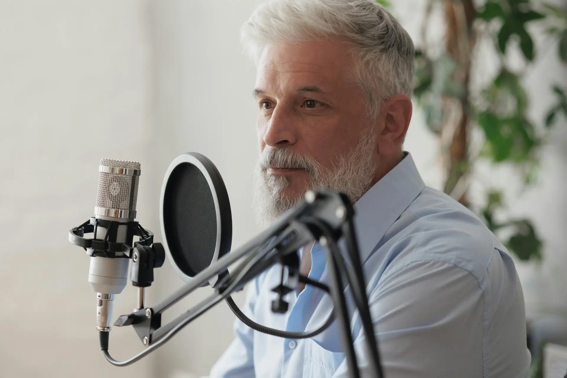 older man with gray hair irecording podcast in recording studio with microphone and headphones